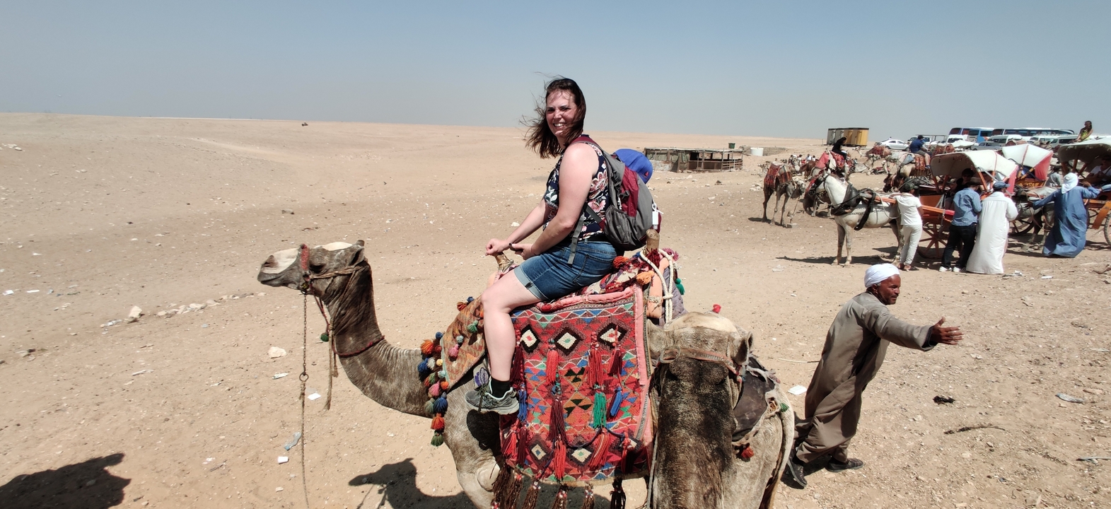Person riding a camel in a desert area with other camels around.