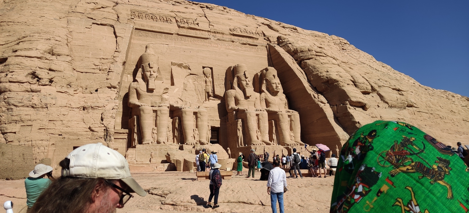 Group of tourists in front of large ancient statues carved into a rocky cliff.