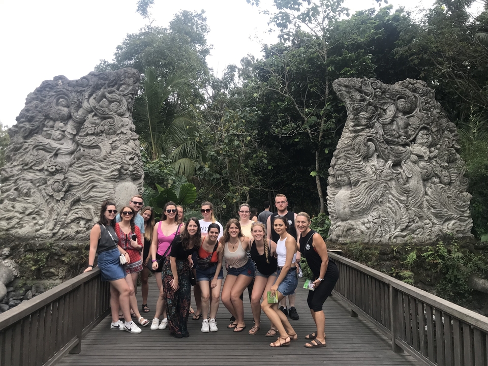 Group of tourists posing in front of detailed sculptures in a lush setting.