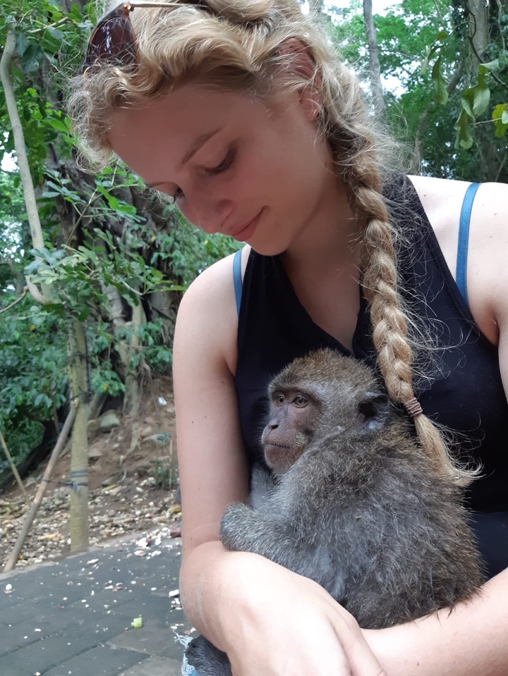 A woman holding a monkey in a lush setting.
