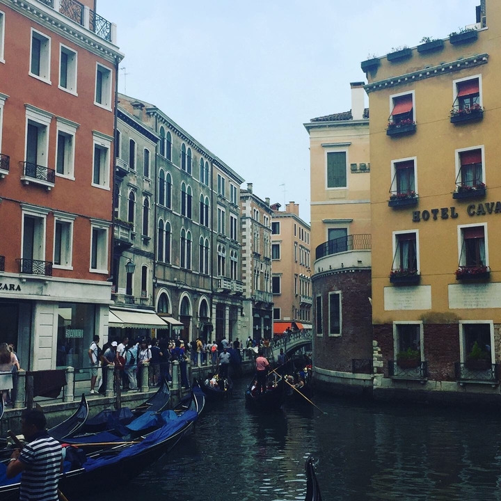 Busy canal street in Venice with a bridge and people walking.