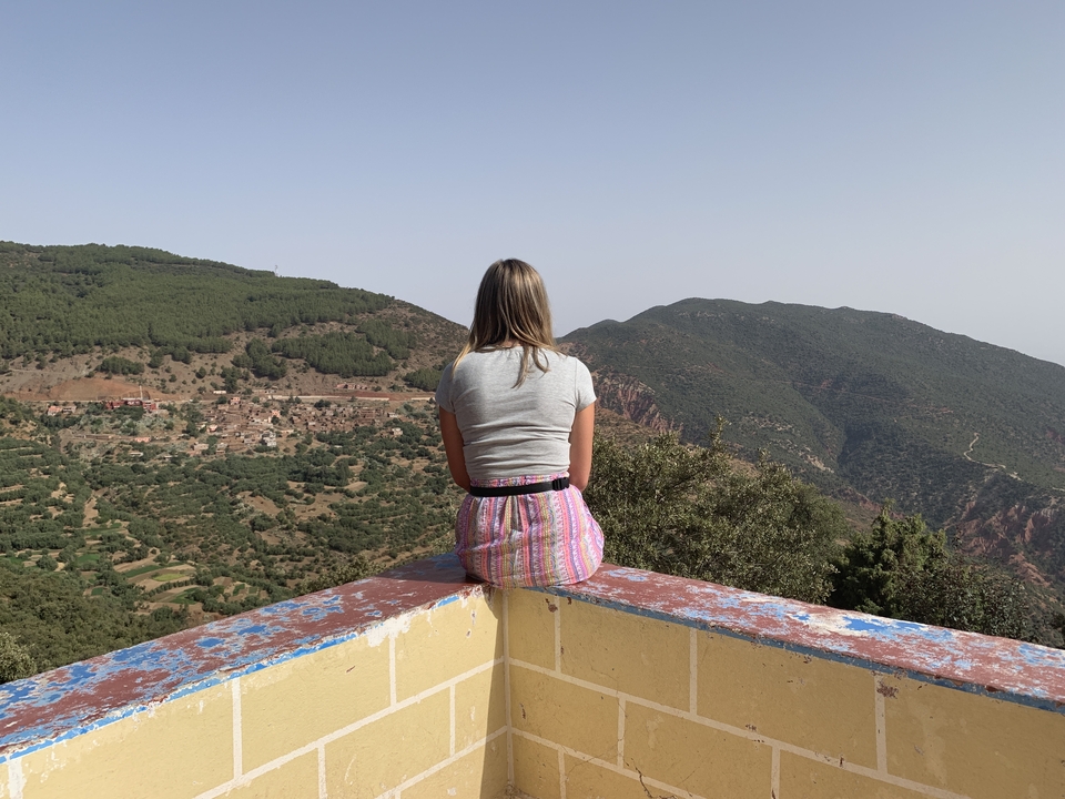 Person sitting on a ledge enjoying a view of hills and villages.