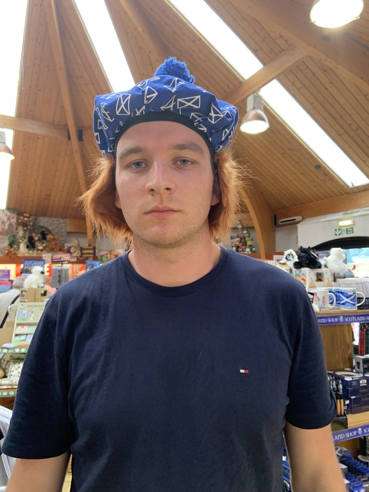 Une personne avec une expression sérieuse à l'intérieur, portant un chapeau souvenir écossais.