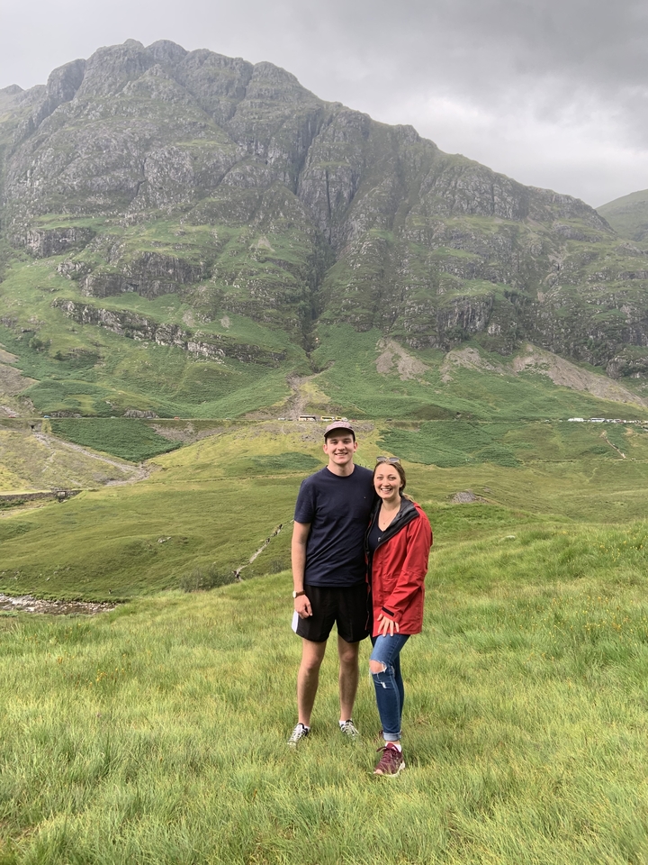 A couple posing on a grassy hill with mountains in the background.