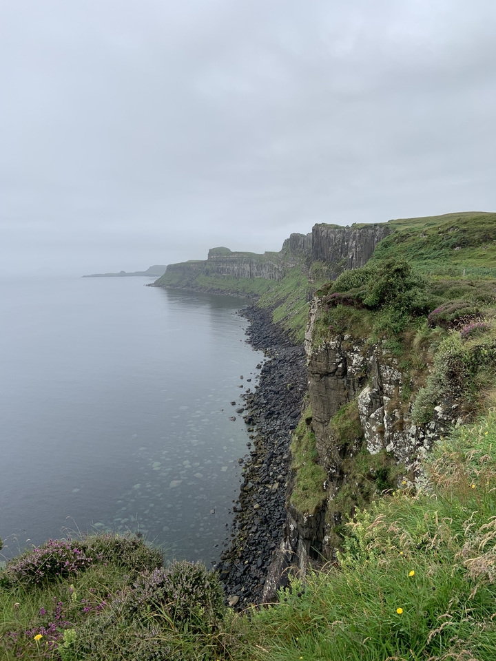 Cliffside with dark rocks leading into the sea under an overcast sky.