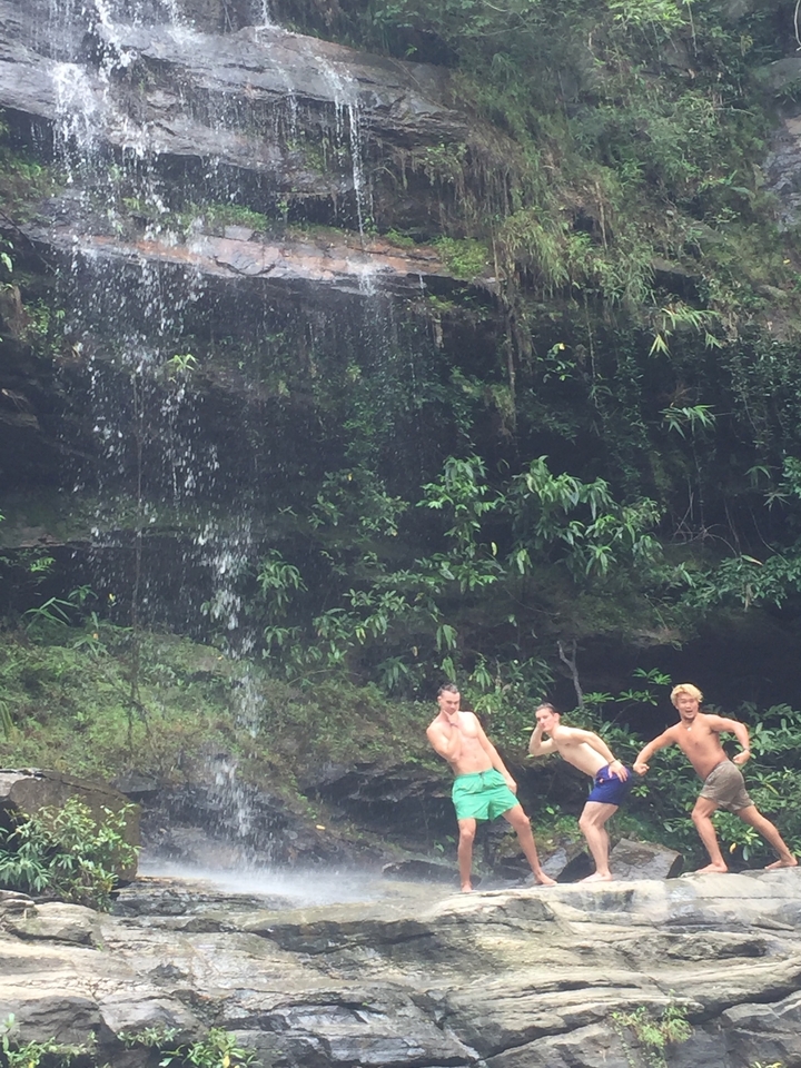 Trois personnes qui prennent des poses amusantes sous une cascade.