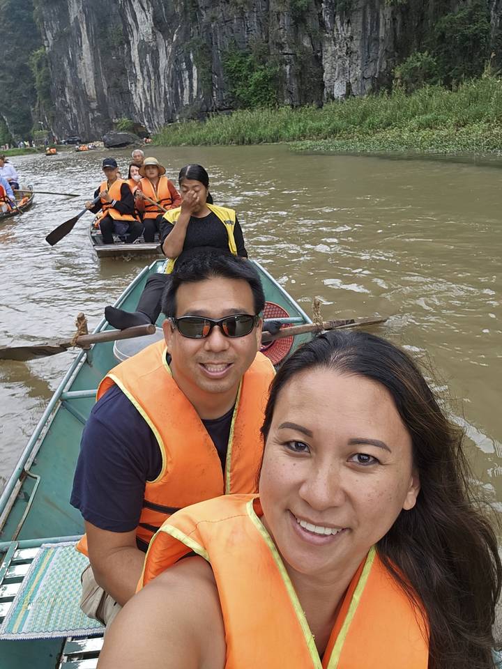 Des personnes en gilets de sauvetage sur un bateau avec un paysage fluvial pittoresque en arrière-plan.