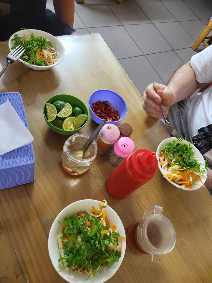 Mains tenant des baguettes au-dessus d'une table avec des plats vietnamiens.