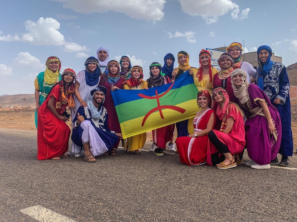 Group wearing colorful traditional outfits holding a flag.