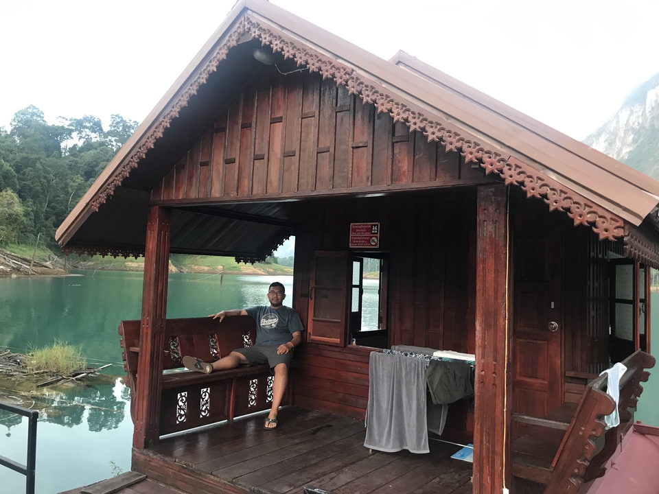 Person sitting on a porch of a wooden cabin by a lake.