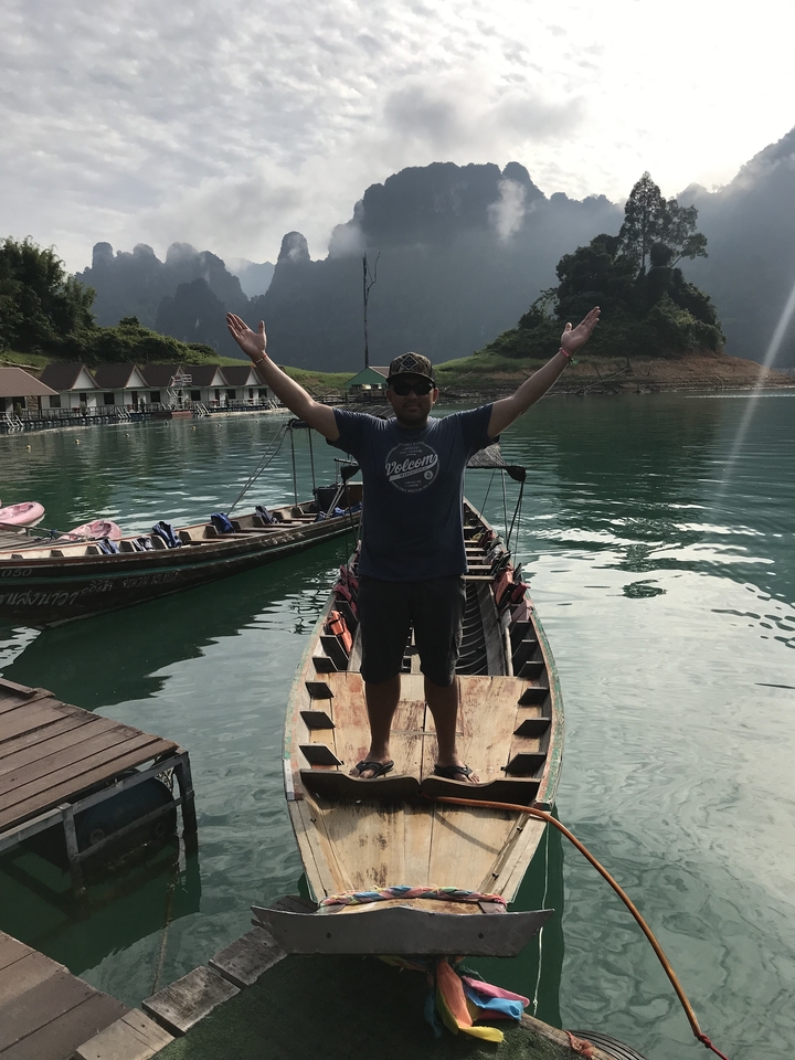 Person standing on a boat with arms raised in a lake.