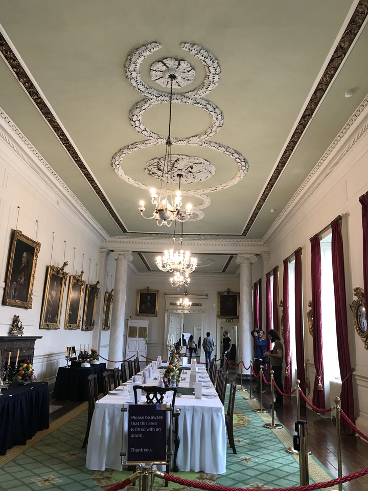 A grand interior with chandeliers and paintings along the walls.