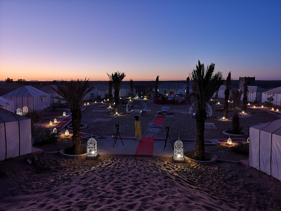 Desert camp illuminated at twilight with tents and palm trees.