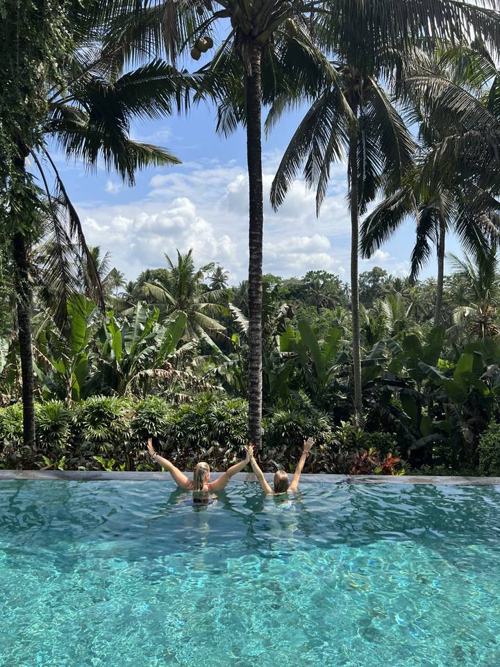 People enjoying a pool surrounded by lush greenery.