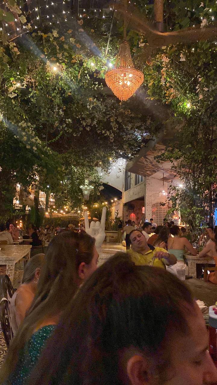 Crowded outdoor restaurant with string lights and chandelier.