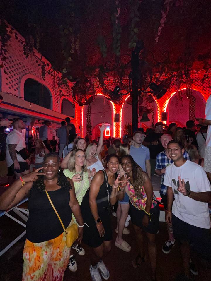 Group of people posing inside a club with red lights.