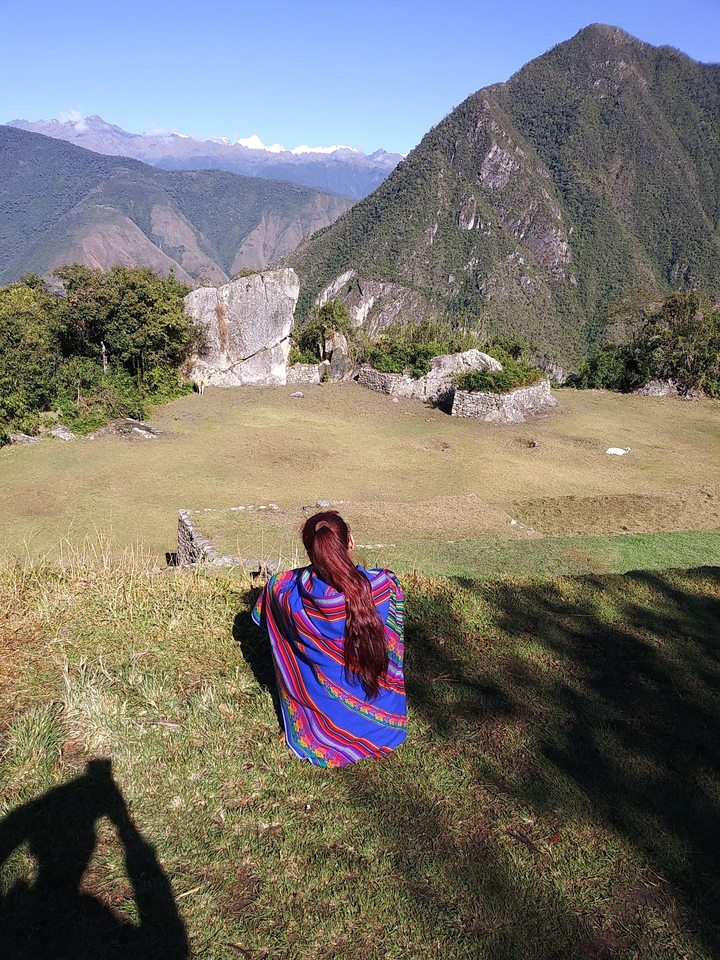 Personne regardant des ruines dans une zone herbeuse avec des montagnes en arrière-plan.