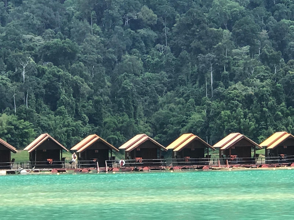 Row of floating huts on a lake with a forest in the background.