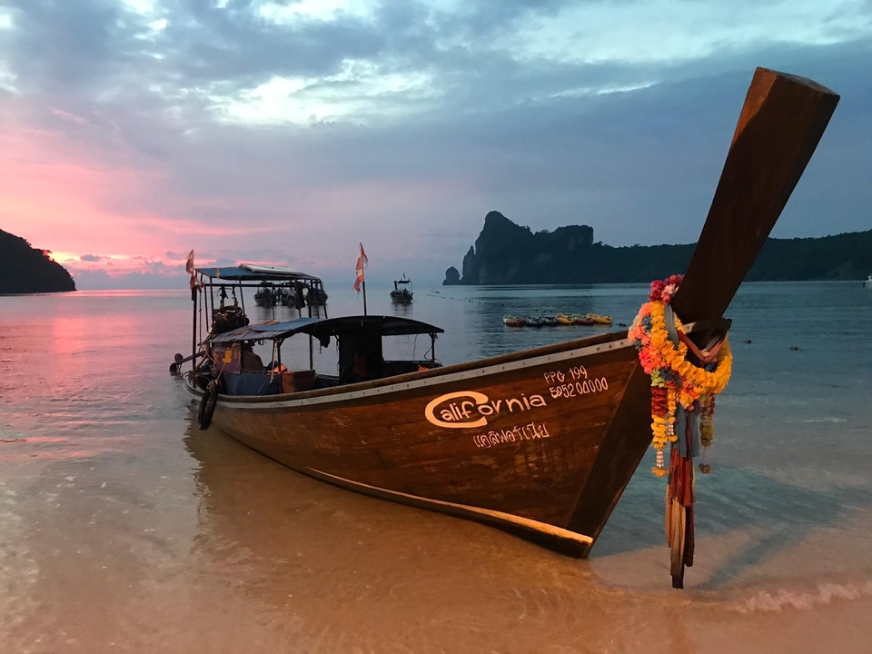 Longtail boat on a beach during a vibrant sunset.