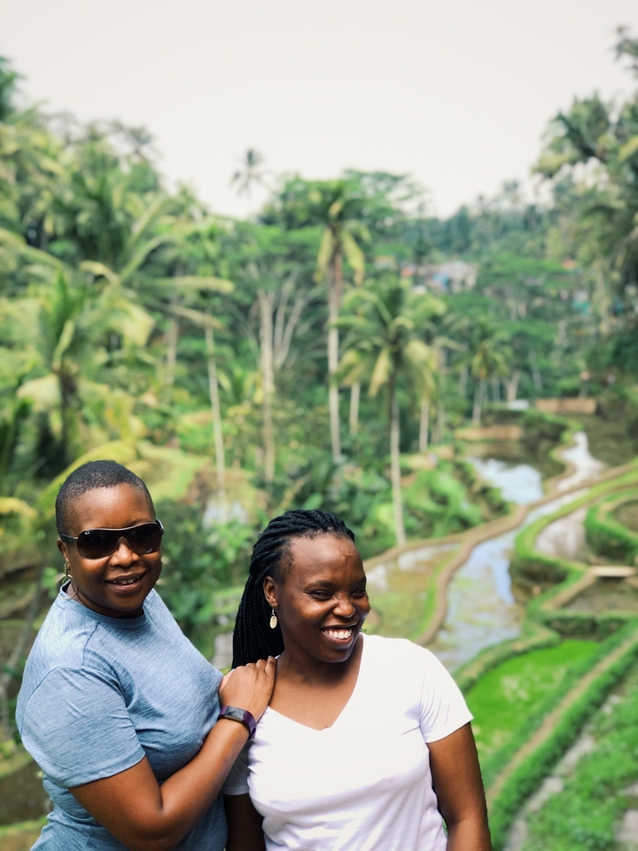 Two people smiling with lush greenery in the background.