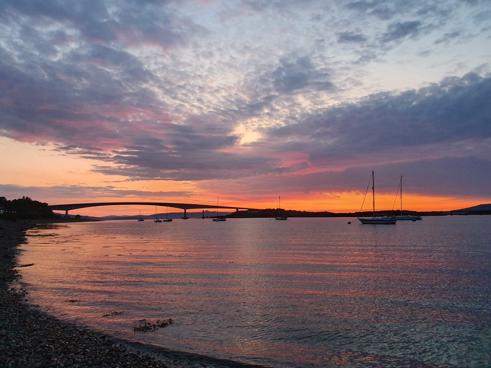 Sunset view of a bridge over a calm water body with boats.