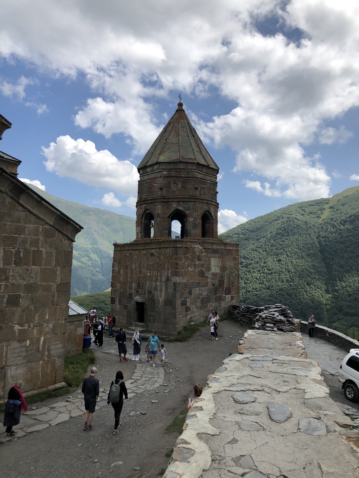A bell tower in a mountainous landscape with people around.