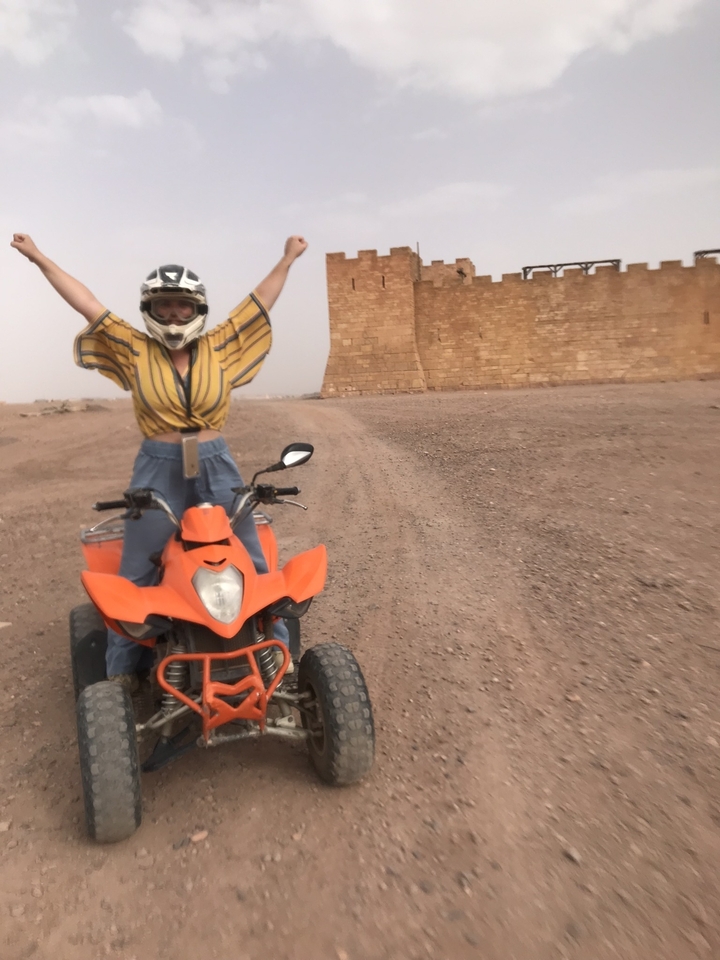 Person on an orange ATV raising arms in excitement in a desert.