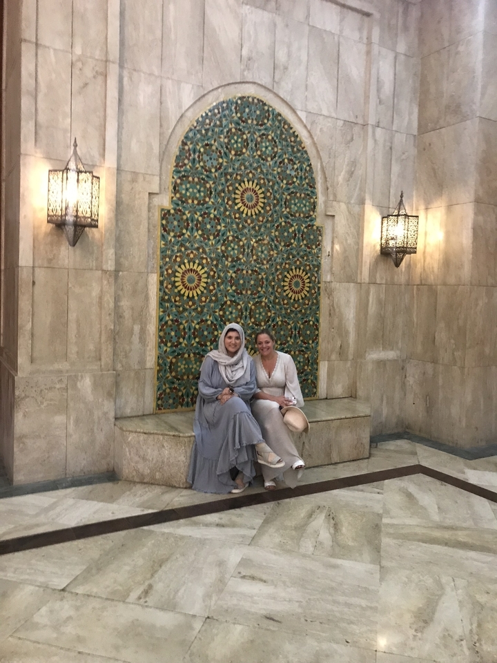 Two women in traditional clothing sitting by a decorative wall.