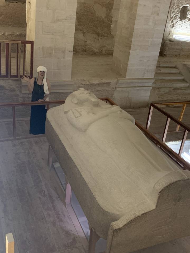 Person standing next to a large stone sarcophagus.