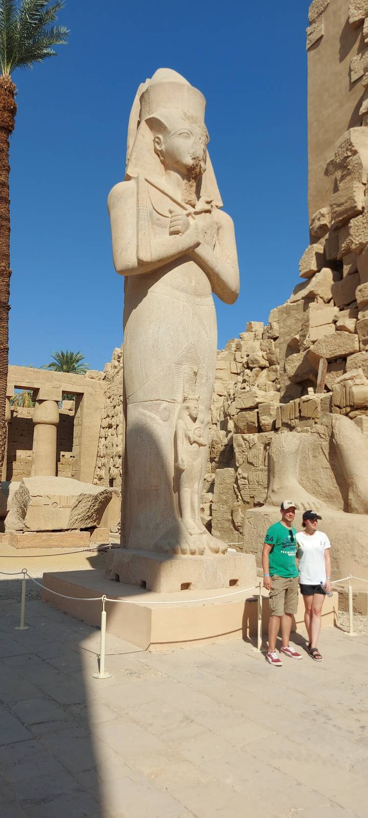 Large ancient statue in a courtyard with two people posing.