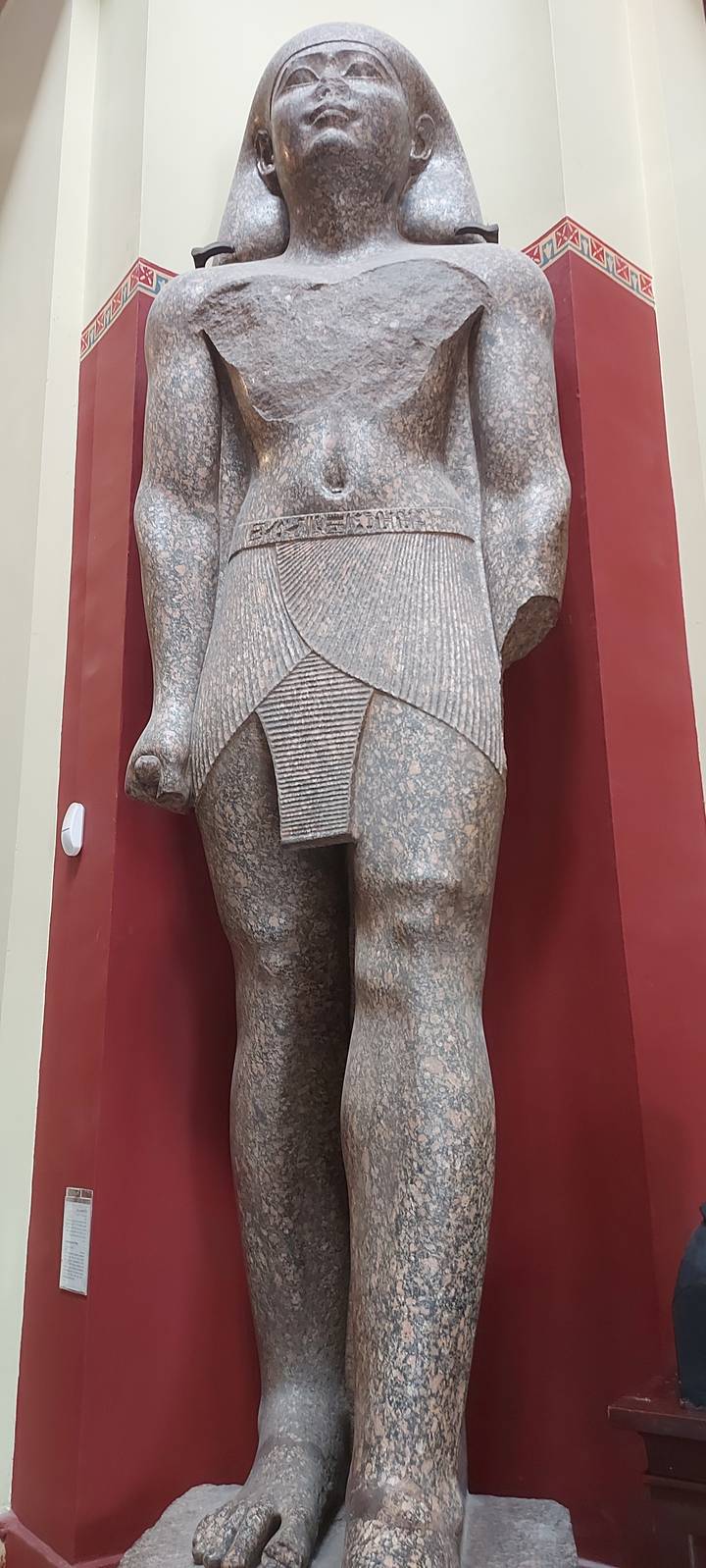 Granite statue of a standing figure in a museum setting.