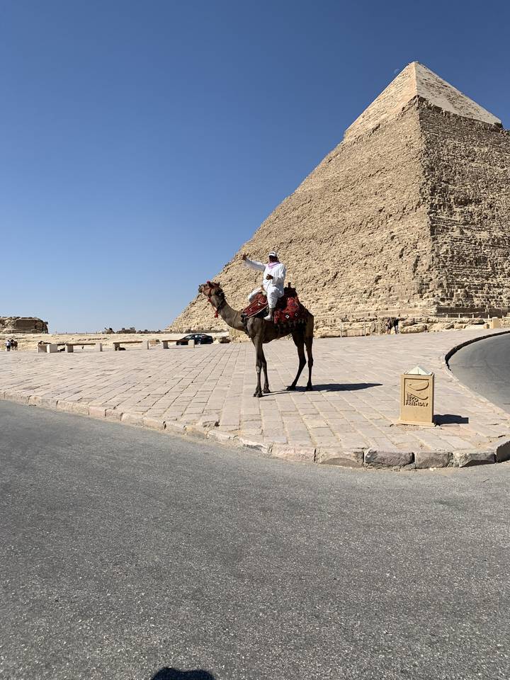 Person riding a camel next to a pyramid.