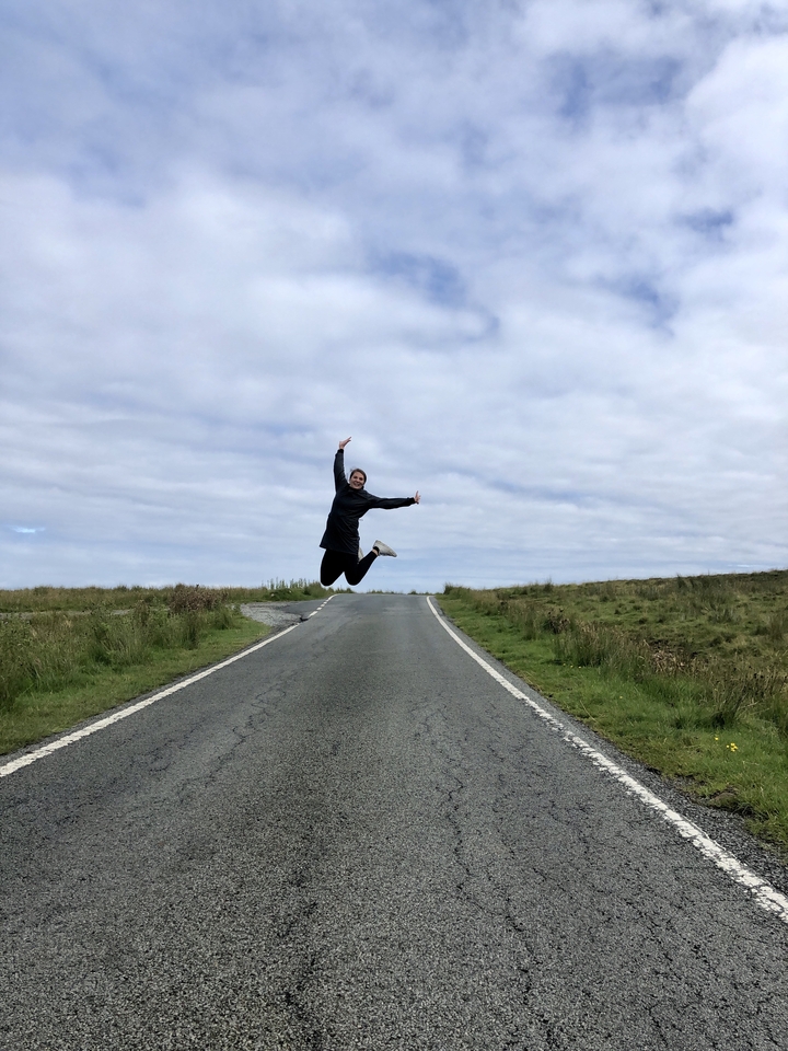Person jumping on an empty road surrounded by fields.