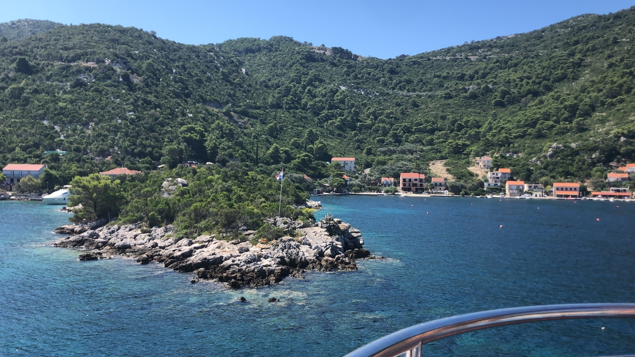 Vue panoramique d'un village côtier avec une végétation luxuriante et une eau bleue.