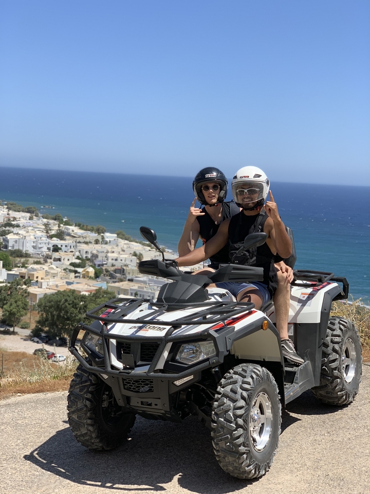 Couple riding an ATV overlooking a seaside village.