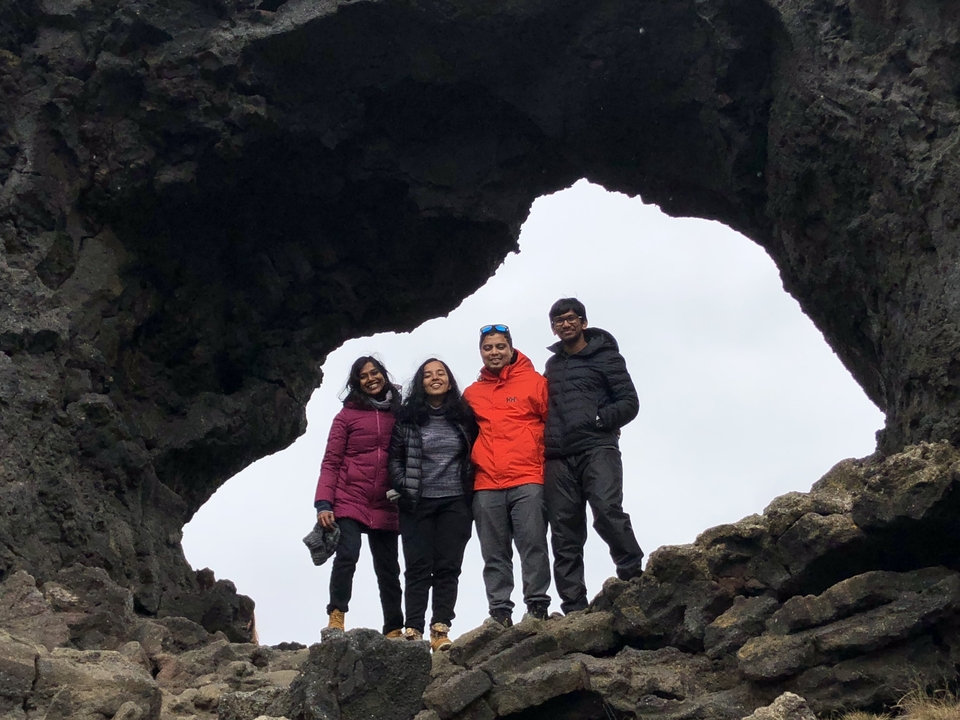 Group of four posing under a rock arch with a cloudy sky.