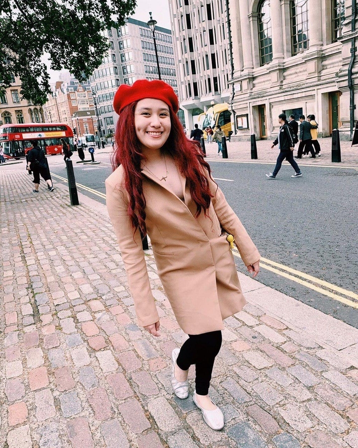 Woman in a coat posing on a cobblestone street with red buses visible.