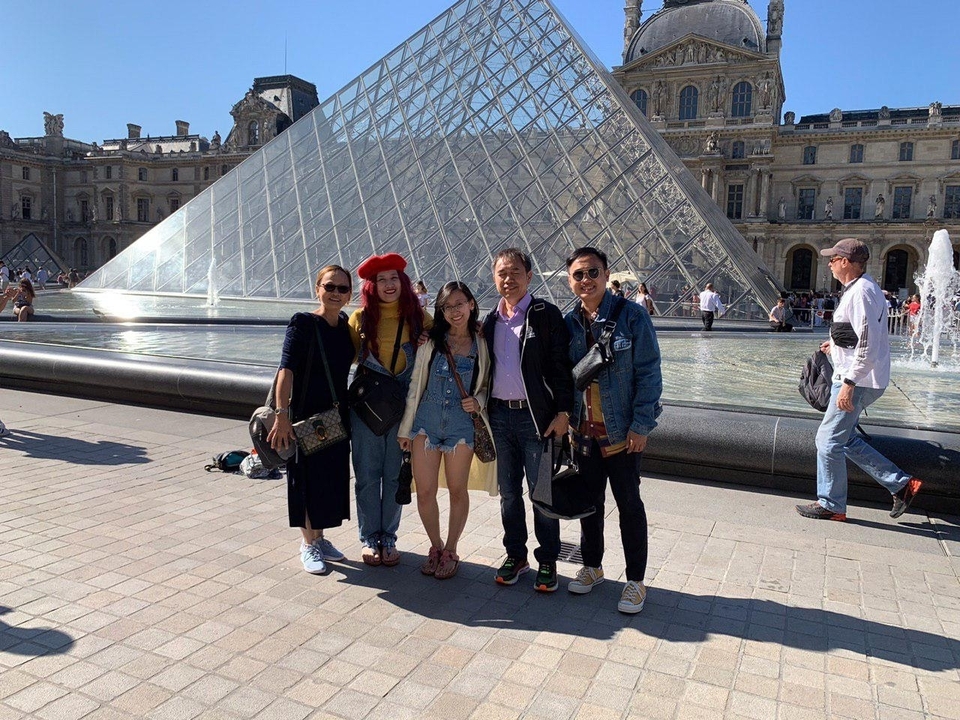 Group of people posing in front of the glass pyramid at the Louvre.