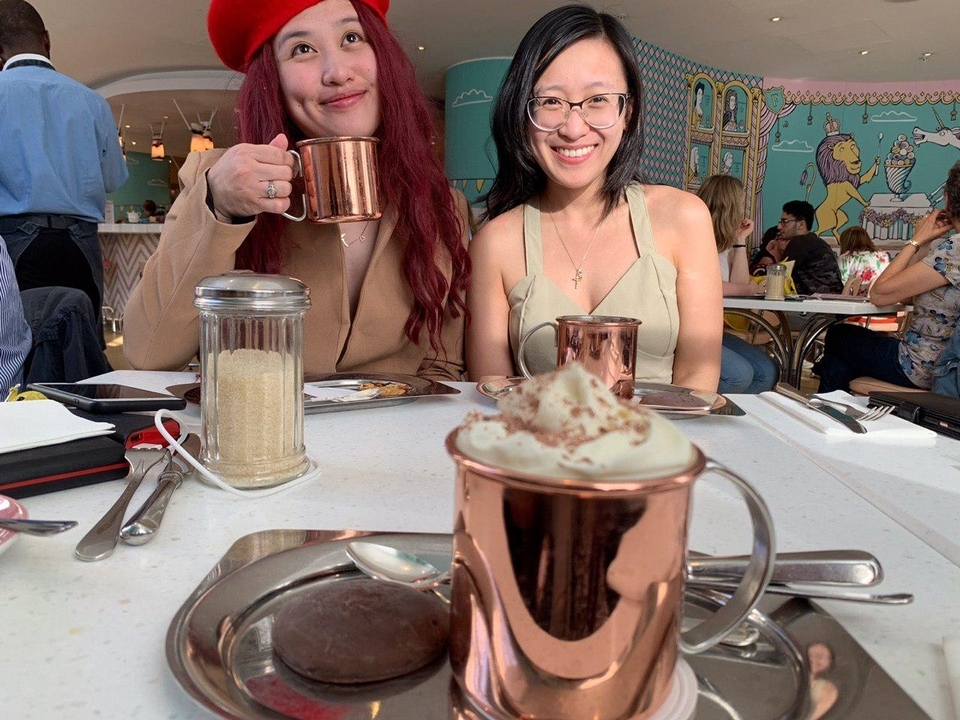 Two women sitting at a cafe table with mugs and sugar.