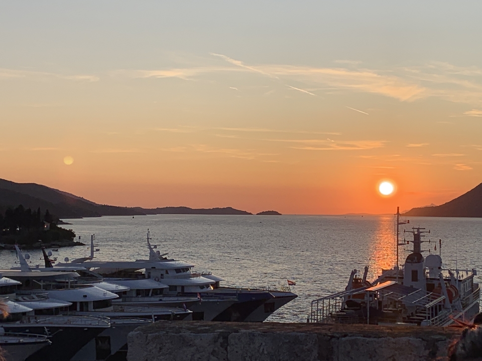 Vue du coucher de soleil sur un port de plaisance avec des yachts et des îles au loin.