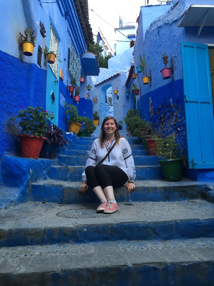 A woman sitting on blue steps in Chefchaouen with colorful pots.