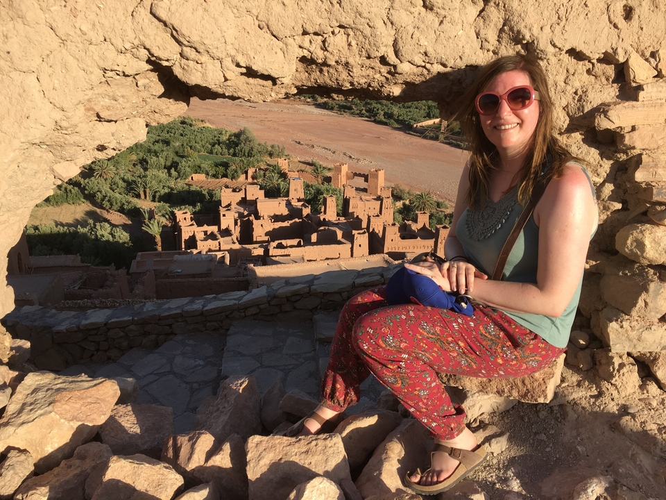 A woman sitting in an ancient fortress with a view of Ait Benhaddou.