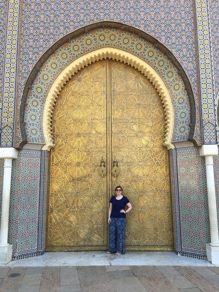 A woman standing in front of a large ornately decorated golden door.