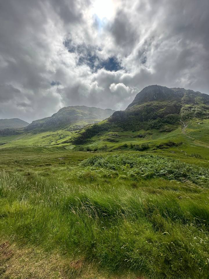 Lush green valley with mountains and cloudy sky.
