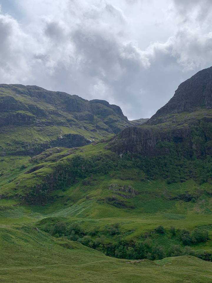 A steep green mountain landscape with cloudy sky.