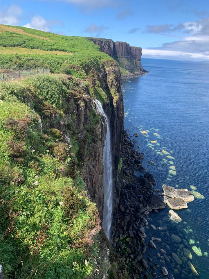 A waterfall falling into the sea surrounded by green cliffs.