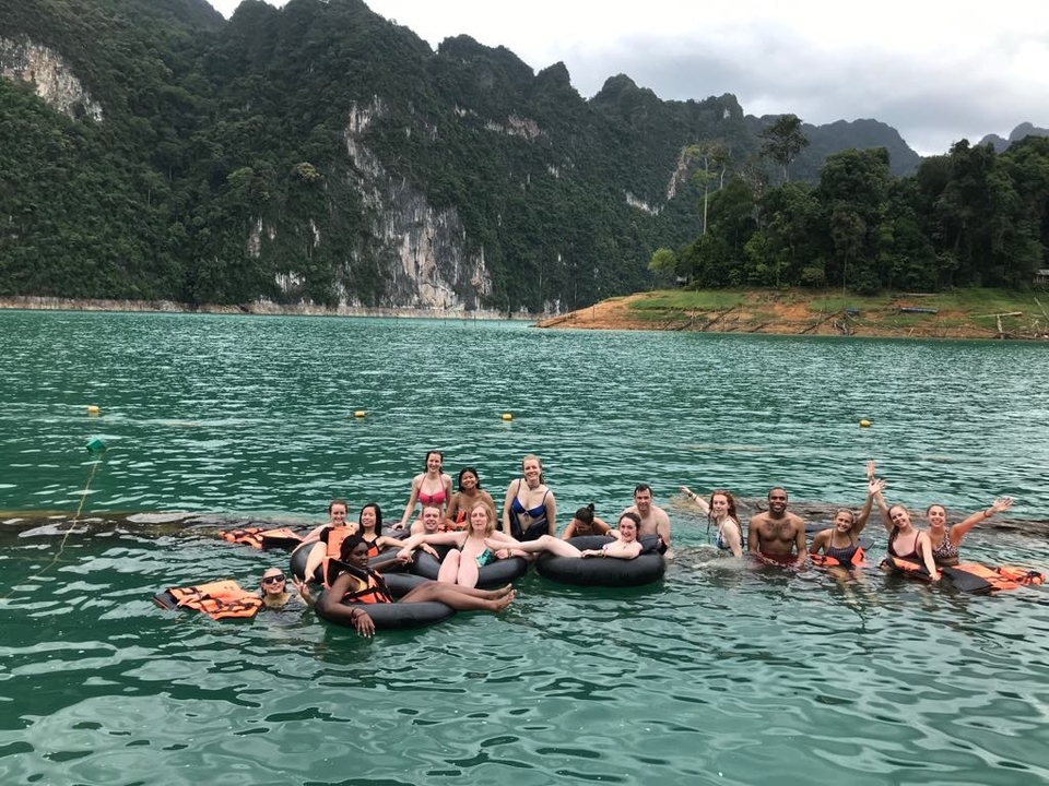 People floating on inner tubes in a scenic lake with mountains.