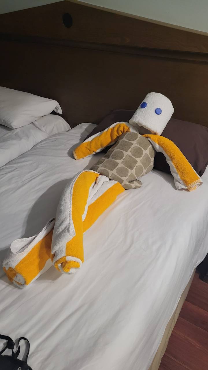 Towel sculpture resembling a person on a bed in a hotel room.