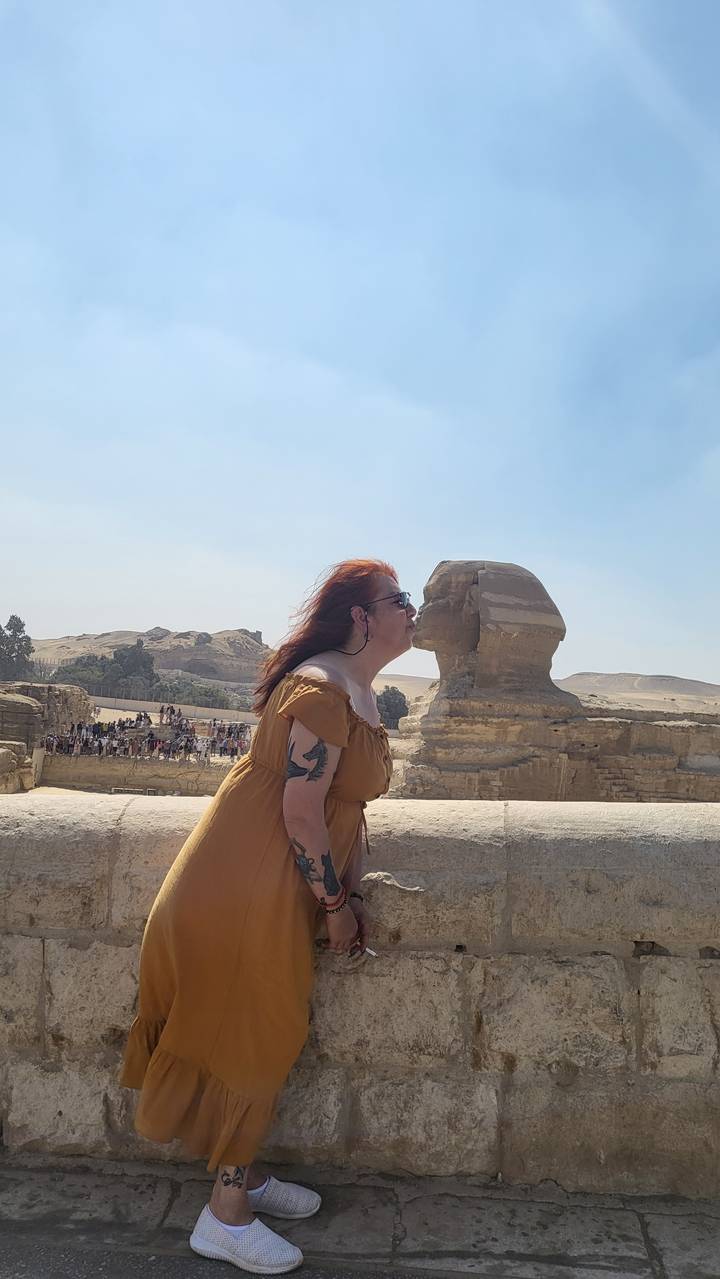 Tourist standing near the Sphinx with desert background.