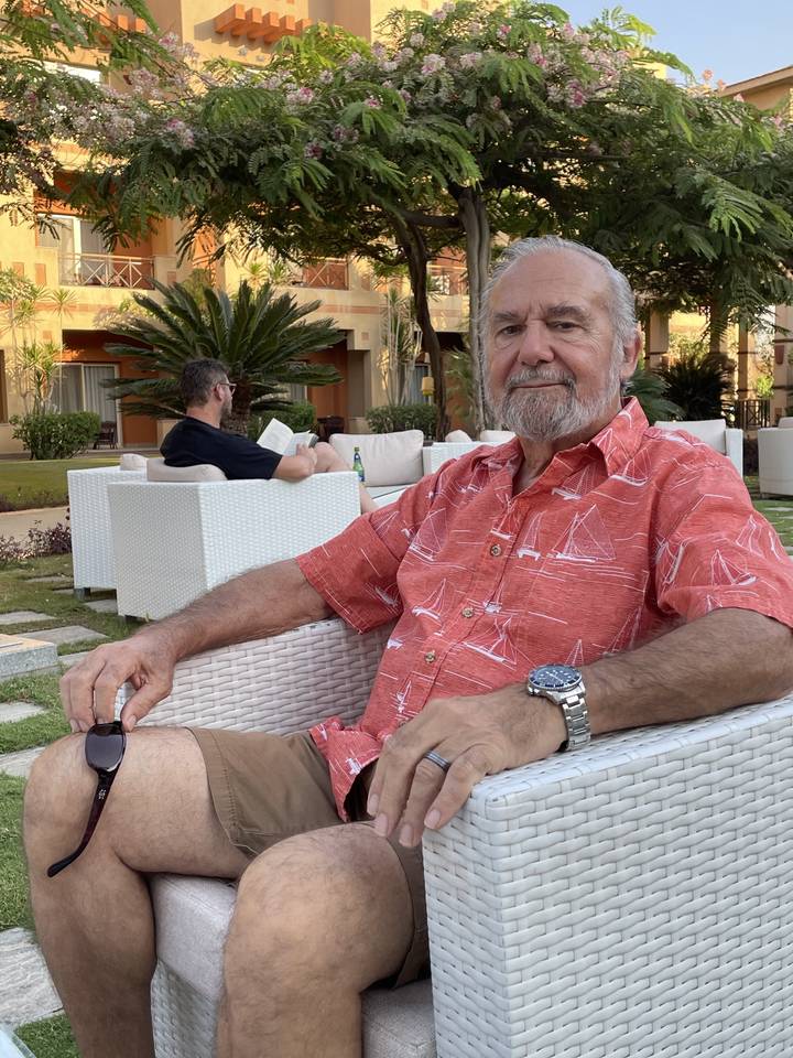 Man sitting on outdoor furniture with drink in hand.